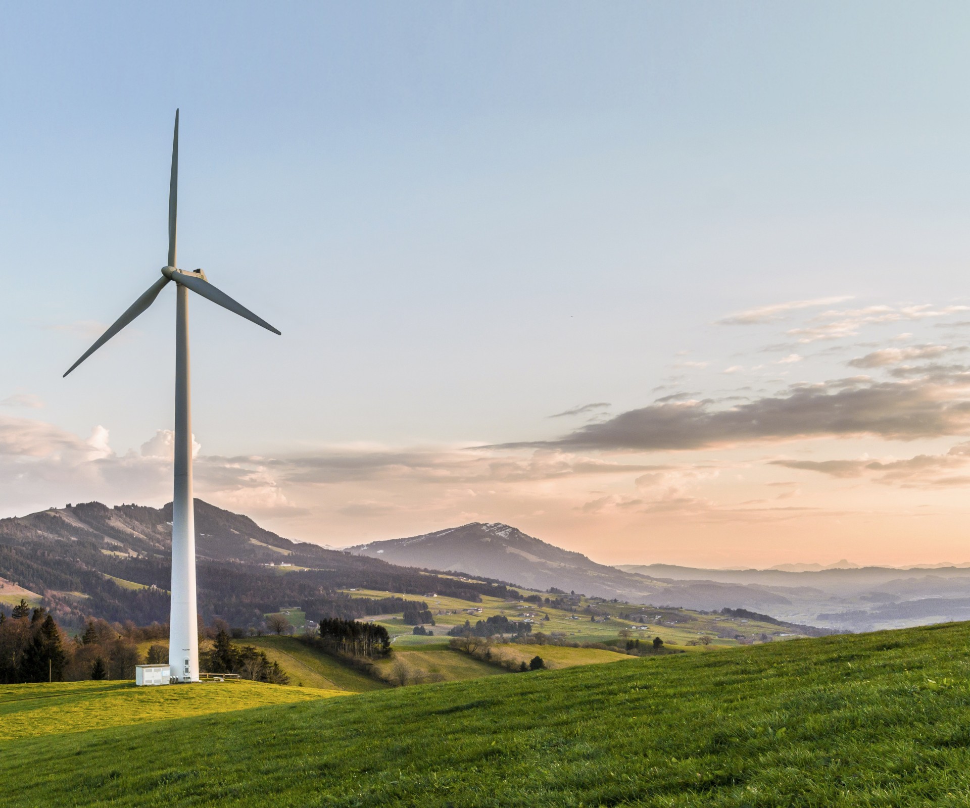 Picture of wind turbine on green lawn with hills in the background and sunset