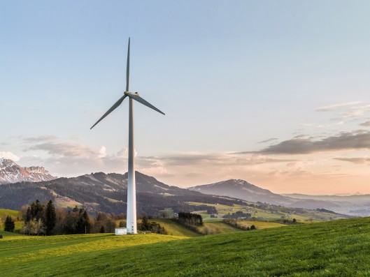 Picture of wind turbine on green lawn with hills in the background and sunset