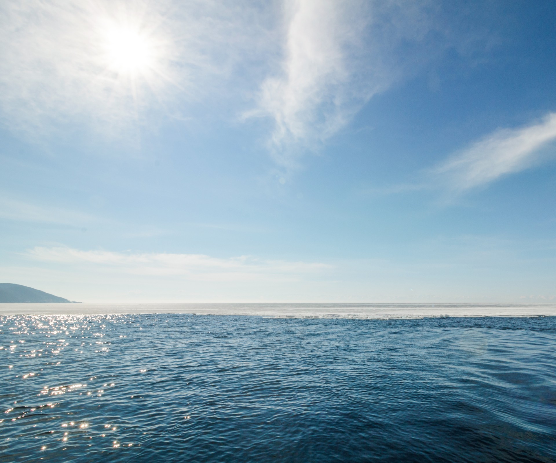 Wide angle view of the sea with sun reflections and blue sky with light veil clouds