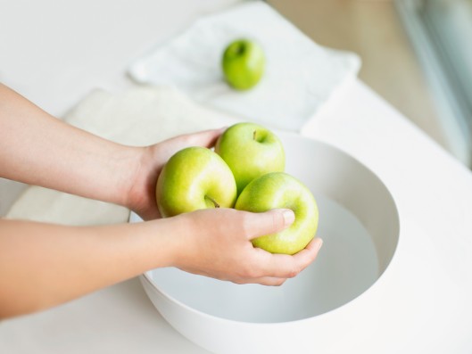 Two hands hold three apples over a bowl of water